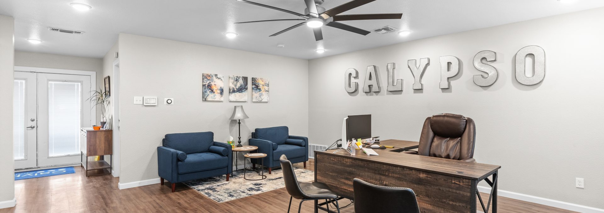 a living room with a ceiling fan and hardwood floors at The Calypso Apartments