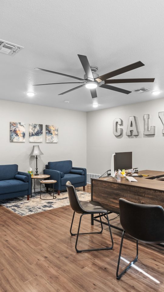 a living room with a ceiling fan and hardwood floors at The Calypso Apartments