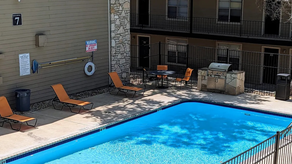 a pool in front of a building with a patio at The Calypso Apartments